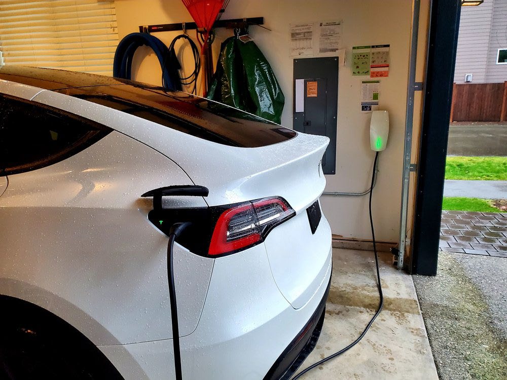 White electric car charging in a garage with a Tesla charging station.